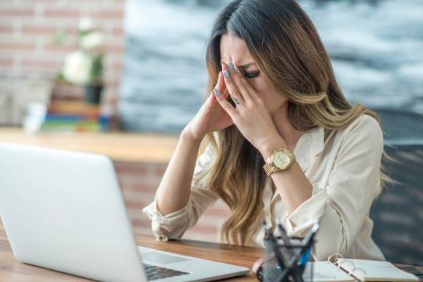 Kobieta po 50-tce odczuwa stres w pracy, siedząc przed komputerem.